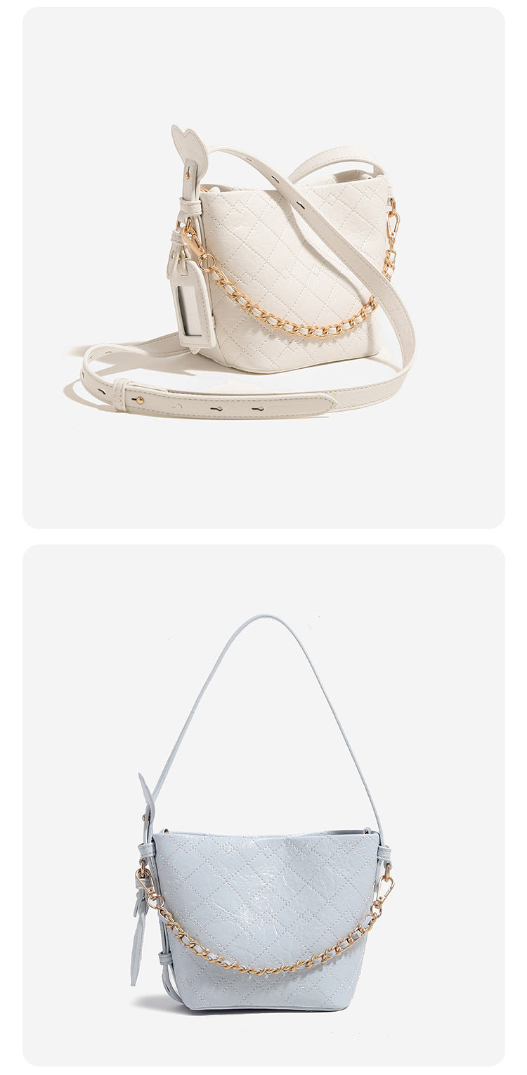 Small diamond-quilted bucket bag with gold-tone chain accent, heart strap detail, hanging tag, and matching zip coin pouch