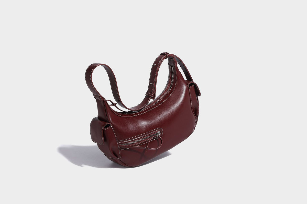 Smooth leather-look crescent shoulder bag with front zip pocket, side flap pockets, adjustable strap, and silver-tone, detail