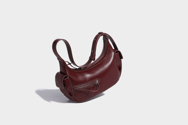 Smooth leather-look crescent shoulder bag with front zip pocket, side flap pockets, adjustable strap, and silver-tone, detail