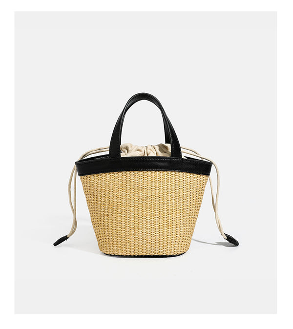 Kleine geflochtene Bucket Bag aus Stroh mit schwarzem Besatz in Lederoptik, zwei oberen Tragegriffen, cremefarbenem Futter mit Kordelzug und seitlichen Kordelverschlüssen