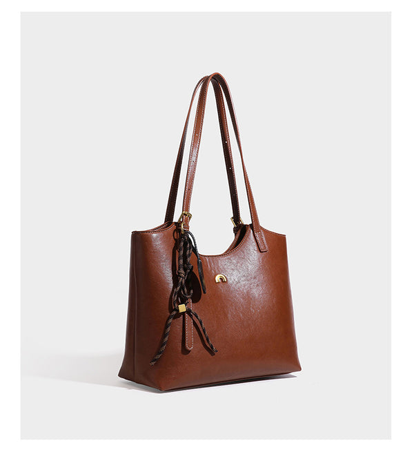 Structured smooth leather-look tote bag with long shoulder strap, gold-tone hardware, and hanging tassel-coin charm, detail
