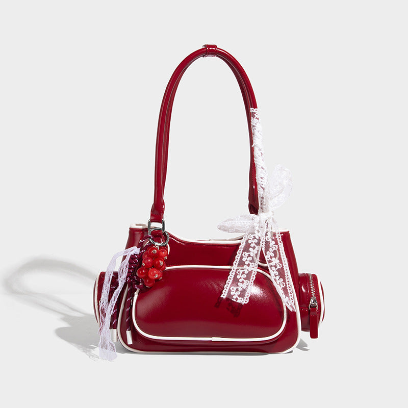 Small structured glossy shoulder bag with white piping trim, lace bow and red bead charm, zip side pockets, and silver-tone