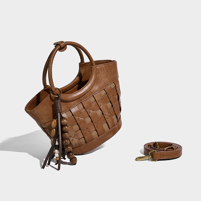 Small woven-panel bucket bag with circular ring handles, beaded tassel charm, and detachable crossbody strap in brown, detail