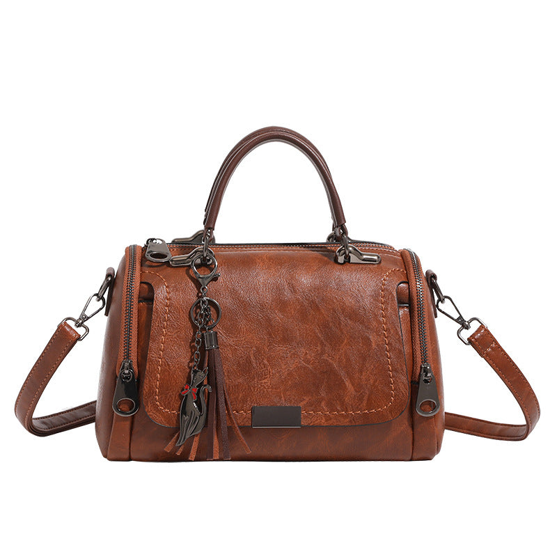 Compact structured barrel bag in distressed leather-look finish with dual top handles, detachable crossbody strap, front zip