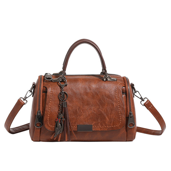 Compact structured barrel bag in distressed leather-look finish with dual top handles, detachable crossbody strap, front zip