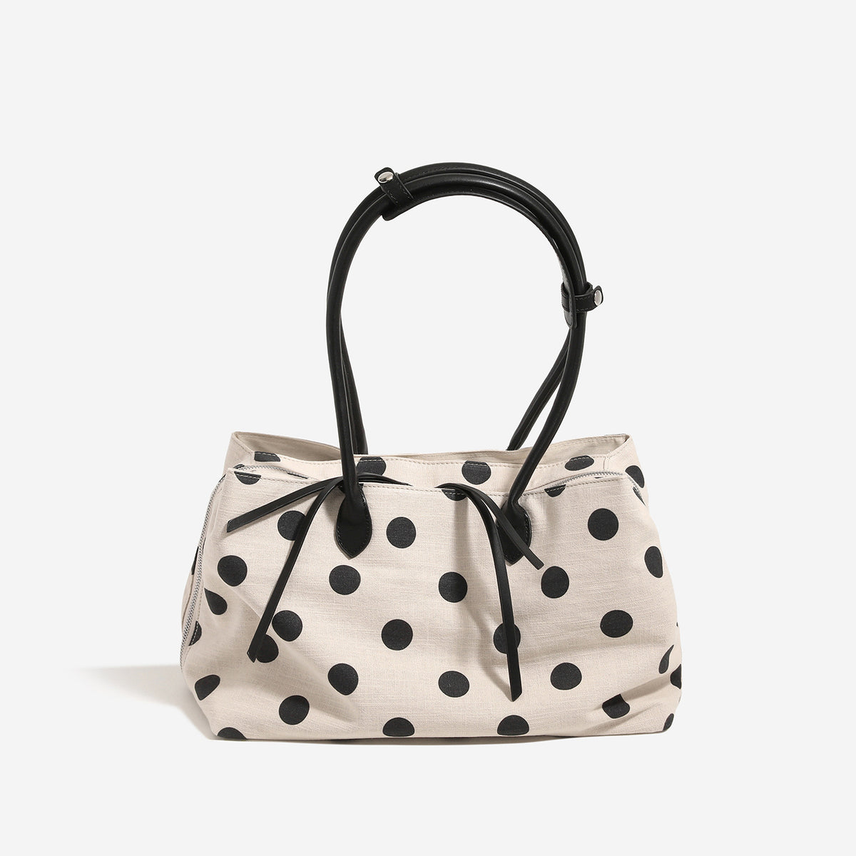 Cream canvas tote bag with black polka dots, rounded leather-look handles, and zip-top closure, front view