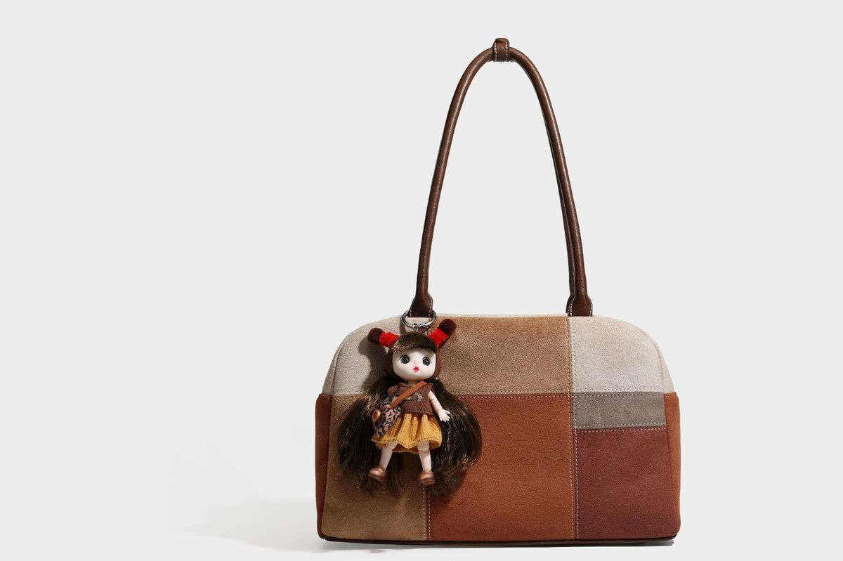 Boxy patchwork suede-look shoulder tote in tan, beige, rust, and brown panels with double brown straps and hanging doll