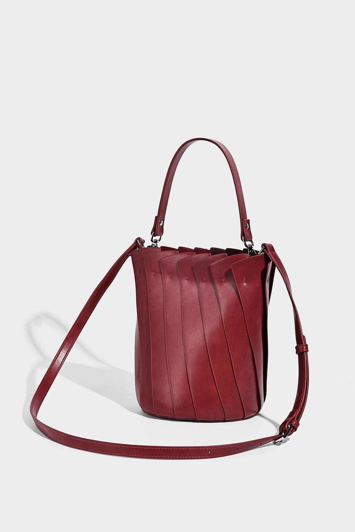 Structured pleated-panel bucket bag with curved top handle and detachable adjustable shoulder strap in smooth matte, detail