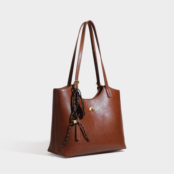 Structured smooth leather-look tote bag with long shoulder strap, gold-tone hardware, and hanging tassel-coin charm, detail