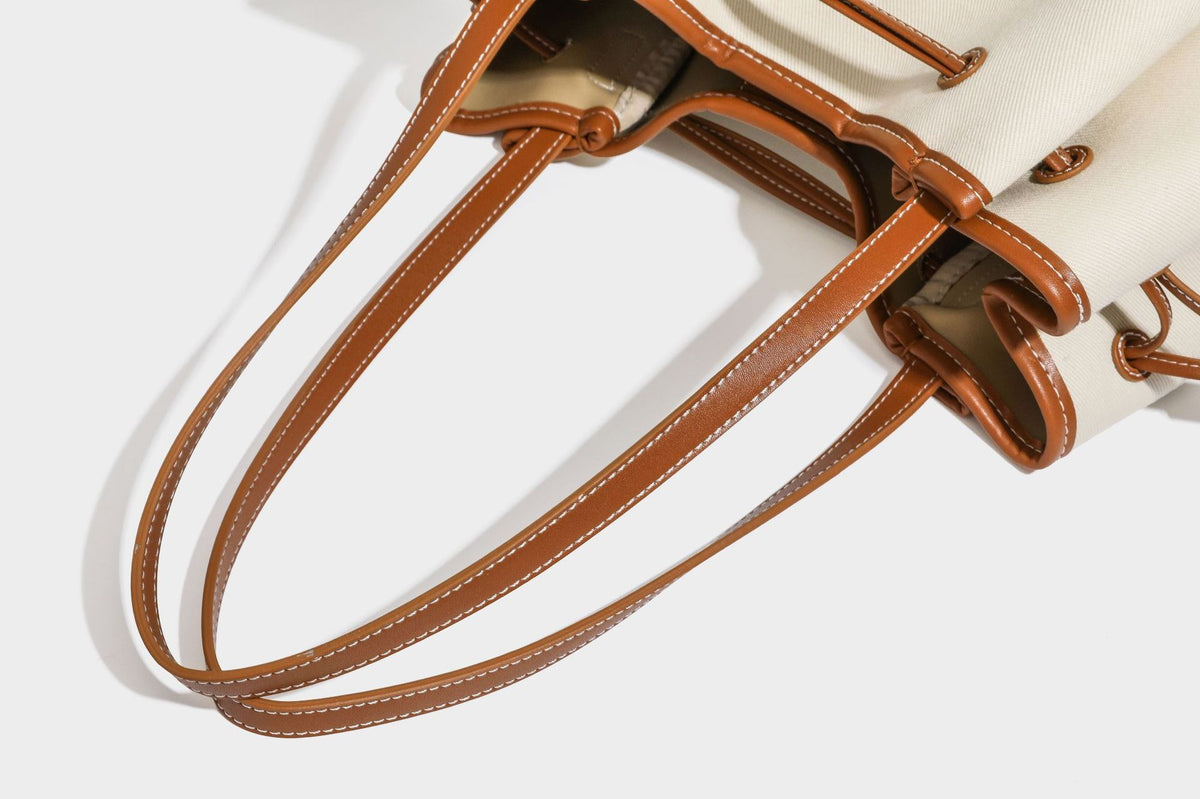 Large cream and navy striped canvas bucket tote bag with tan leather-look trim, drawstring closure, and double shoulder