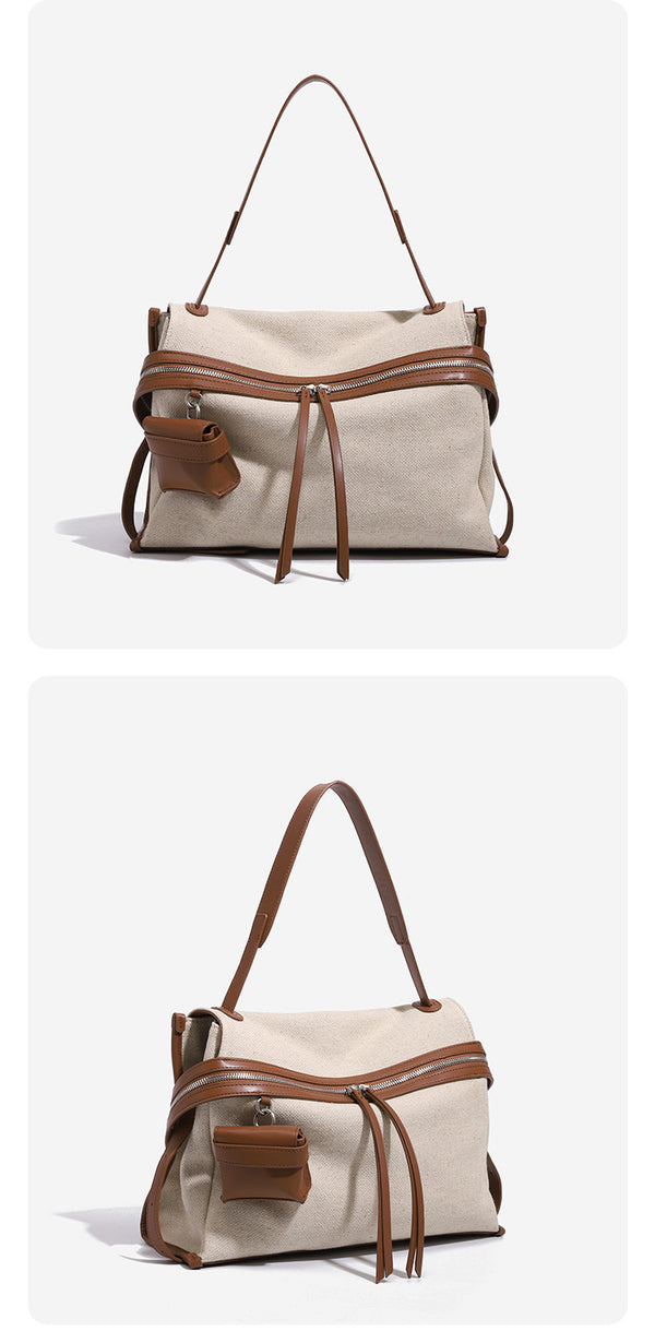 Cream canvas zip-top shoulder bag with cognac leather-look trim, dual zipper, attached mini pouch, and tassel strap ties
