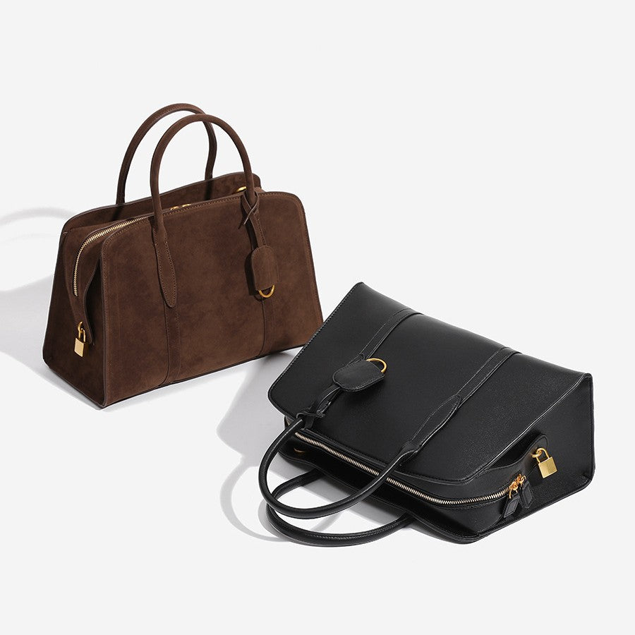 Structured trapezoid Boston satchel bag with dual top handles, gold-tone lock charm, and top zip closure, front view