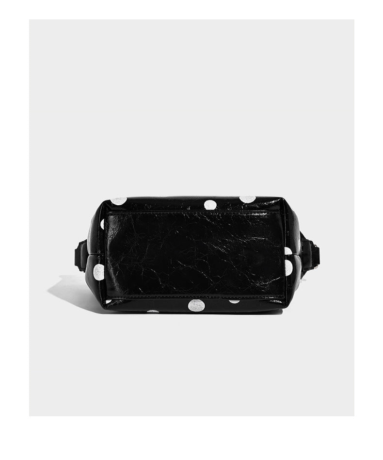 Schultertasche in glänzender Lederoptik mit Punktemuster, aufgesetztem Mini-Fronttäschchen, Reißverschluss oben und verstellbarem Riemen, Detailansicht