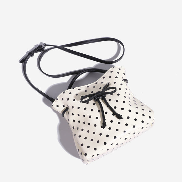 Cream white polka-dot drawstring bucket bag with black leather-look top handle and bow-tied cord closure, detail view 4