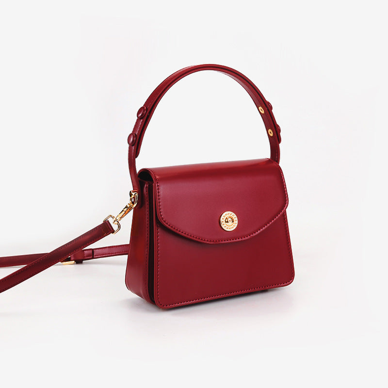 Kleine strukturierte Henkeltasche mit Überschlag in tiefem Rot, glatter Lederoptik, goldfarbenem Drehverschluss, kurzem Henkel und