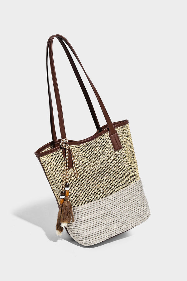 Woven straw-look tote bag in tan and cream with dark brown leather-look trim, long flat shoulder straps, and tassel bead