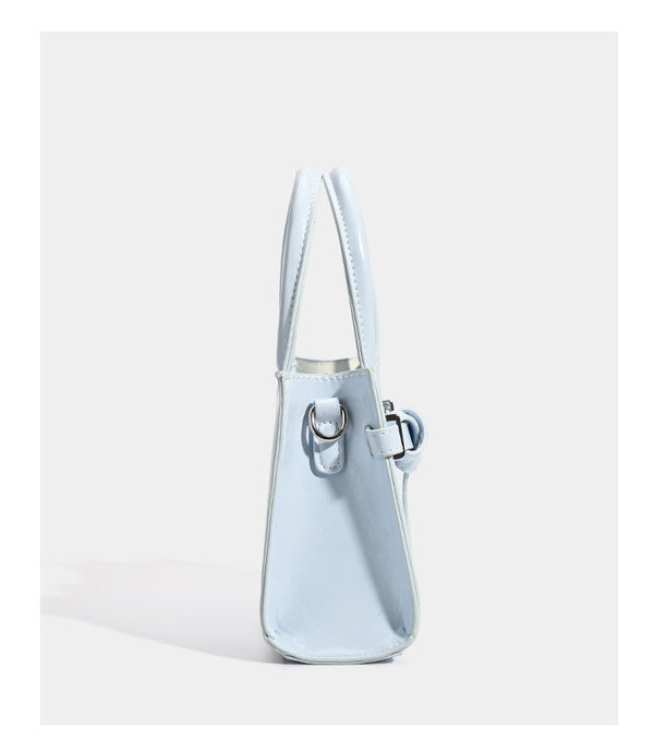 Small structured trapezoid mini top-handle bag with front belt-knot buckle detail and glossy leather-look finish, detail view