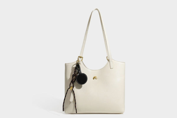 Structured smooth leather-look tote bag with long shoulder strap, gold-tone hardware, and hanging tassel-coin charm, detail