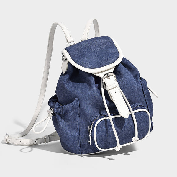 Compact denim drawstring backpack with white leather-look piping, flap-top buckle closure, front zip pocket, and silver-tone