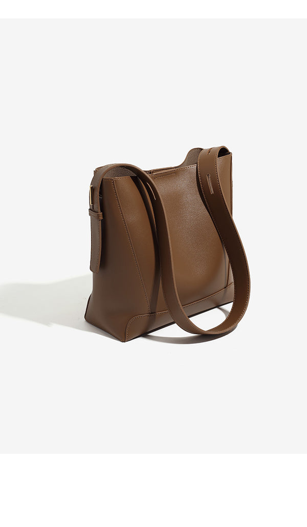 Structured smooth leather-look bucket shoulder bag with long adjustable strap and gold-tone buckle hardware in brown, detail