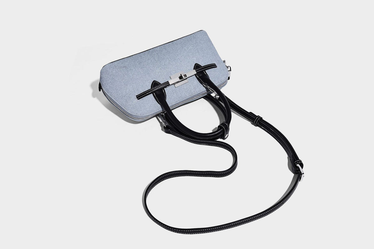 Compact structured satchel in light blue denim-look fabric with black leather-look trim, silver turn-lock closure, rolled
