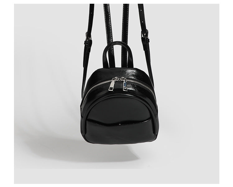 Kompakte, abgerundete Mini-Rucksacktasche mit glänzender Oberfläche in Lederoptik, Reißverschluss oben, Fronttasche, Tragegriff oben und, Detail