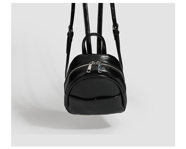 Kompakte, abgerundete Mini-Rucksacktasche mit glänzender Oberfläche in Lederoptik, Reißverschluss oben, Fronttasche, Tragegriff oben und, Detail
