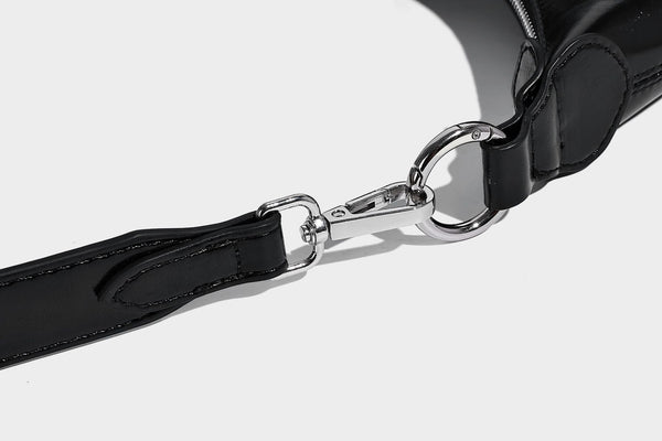 Glossy black slouchy hobo shoulder bag with silver-tone hardware, belt-style grommet strap at base, and long adjustable
