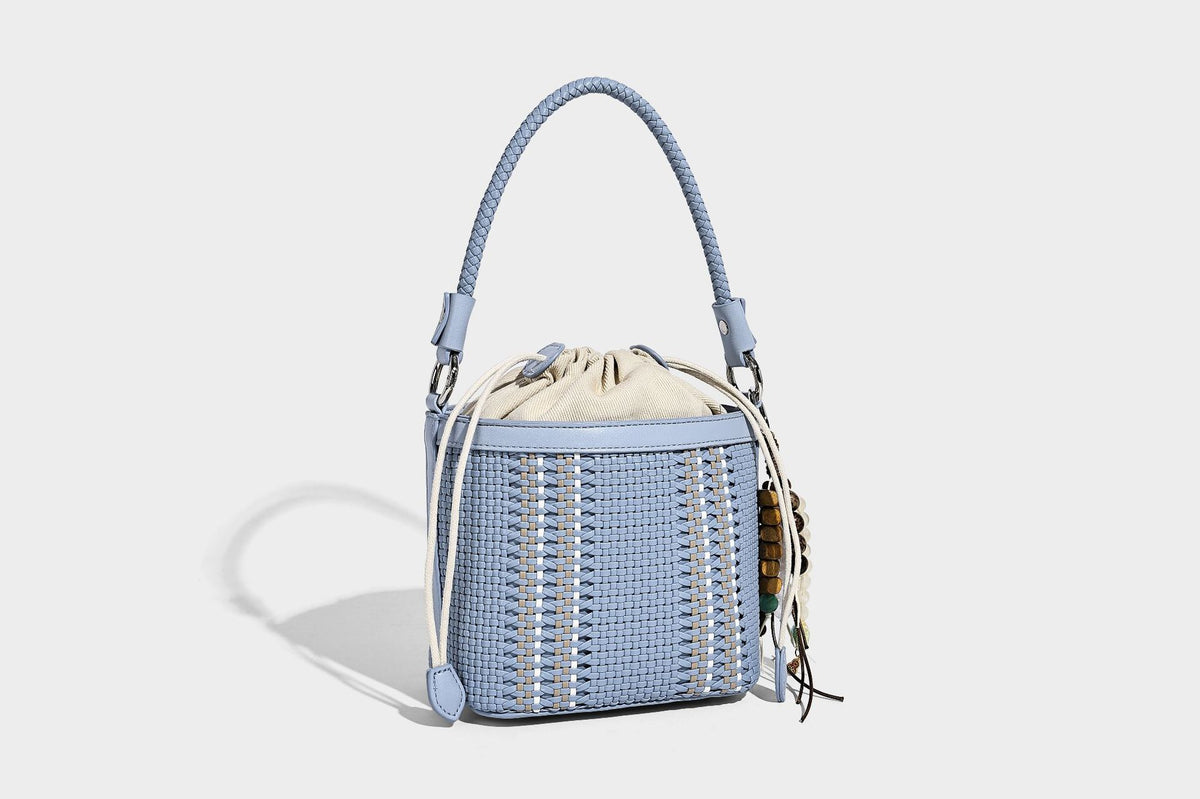 Small woven bucket bag with drawstring top, braided handle, detachable crossbody strap, and silver-tone ring hardware, detail