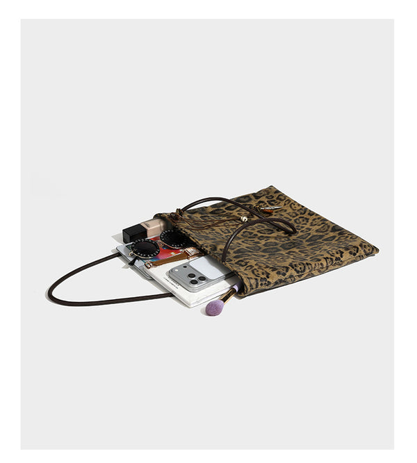 Large leopard print shoulder tote bag in tan and brown with slim dark straps and dangling beaded charm hardware, detail view