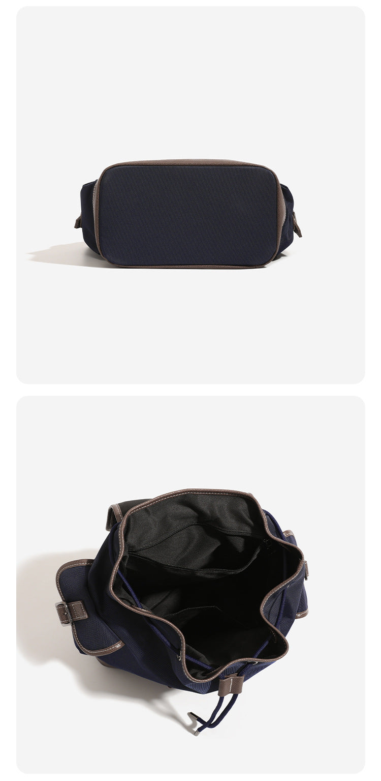 Deep navy canvas backpack with brown textured leather-look trim, drawstring flap closure, buckle-strap front detail, and