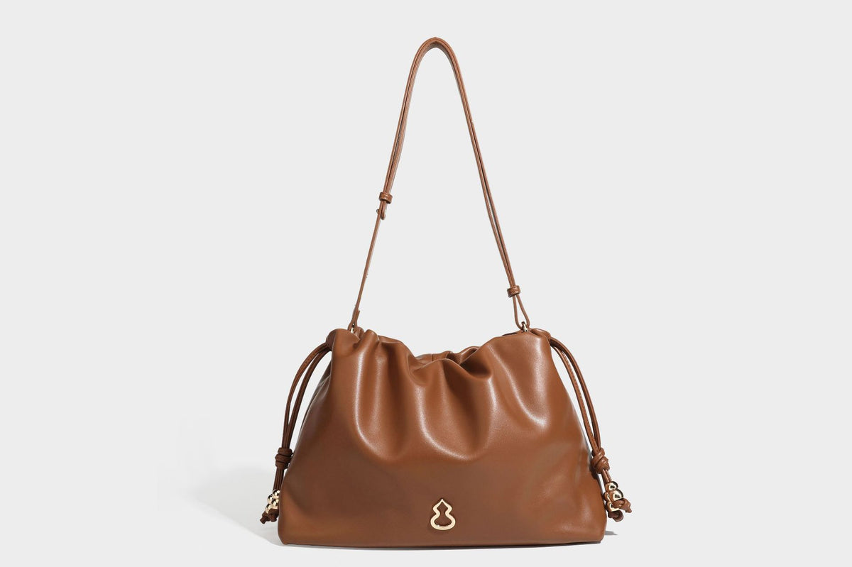 Slouchy ruched drawstring shoulder bag in smooth leather-look finish with gold-tone emblem and slim adjustable strap, detail