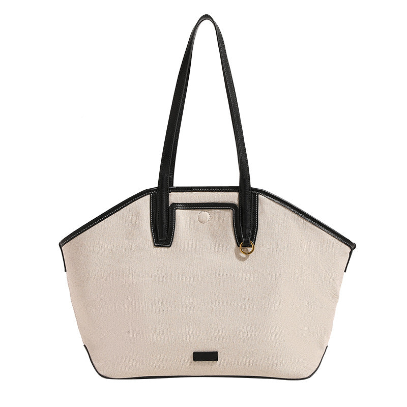 Trapezförmige Tote-Bag aus cremefarbenem Canvas mit schwarzem Besatz in Lederoptik, zwei Schulterriemen und goldfarbenen Ringbeschlägen, Detailansicht
