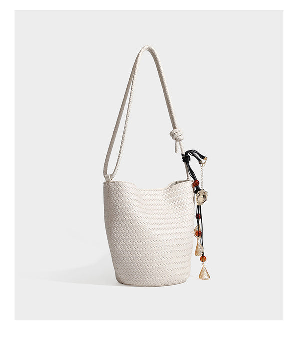 Olive green woven leather-look bucket bag with braided crossbody strap, knotted adjustment, and gold-tone tassel charm with