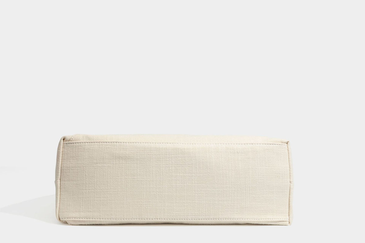 Soft slouchy cream canvas shoulder tote with braided brown and green cord handle, gold-tone ring hardware, and tassel trim