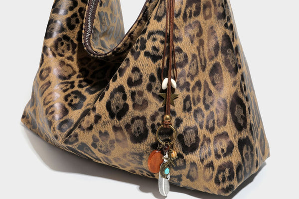 Slouchy leopard print hobo shoulder bag with glossy coated finish, top zipper closure, dark brown trim, and dangling charm