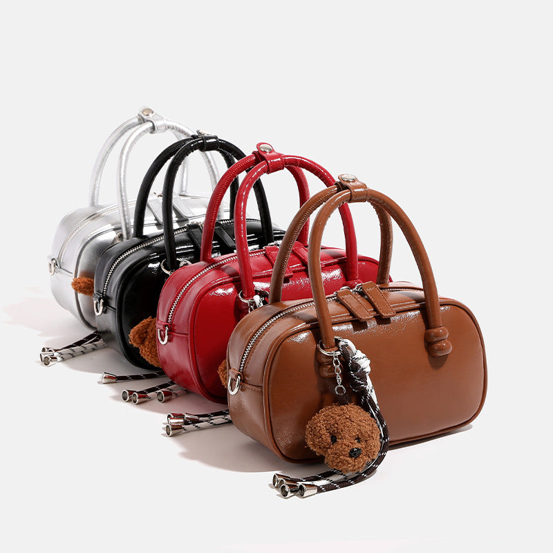 Glossy leather-look mini bowling barrel bag with dual top handles, detachable braided strap, and teddy bear charm, detail