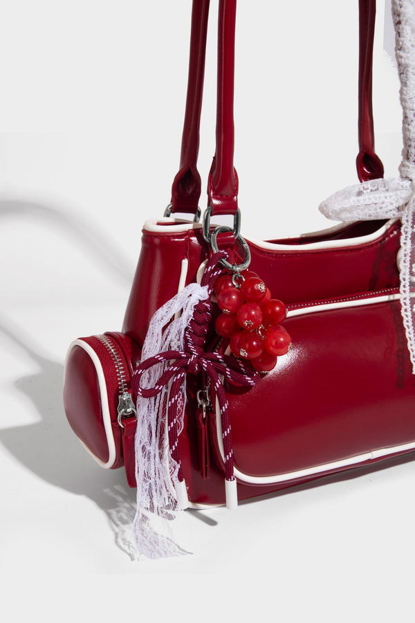 Kleine, formstabile, glänzende Schultertasche mit weißer Paspelierung, Spitzenschleife und Anhänger mit roter Perle, seitlichen Reißverschlusstaschen und silberfarbenem