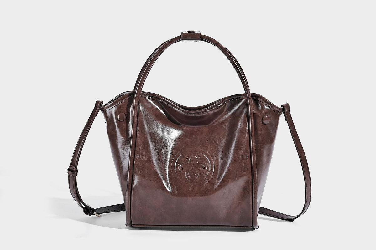 Glossy leather-look structured tote bag with rounded top handles, detachable shoulder strap, embossed front emblem, and side