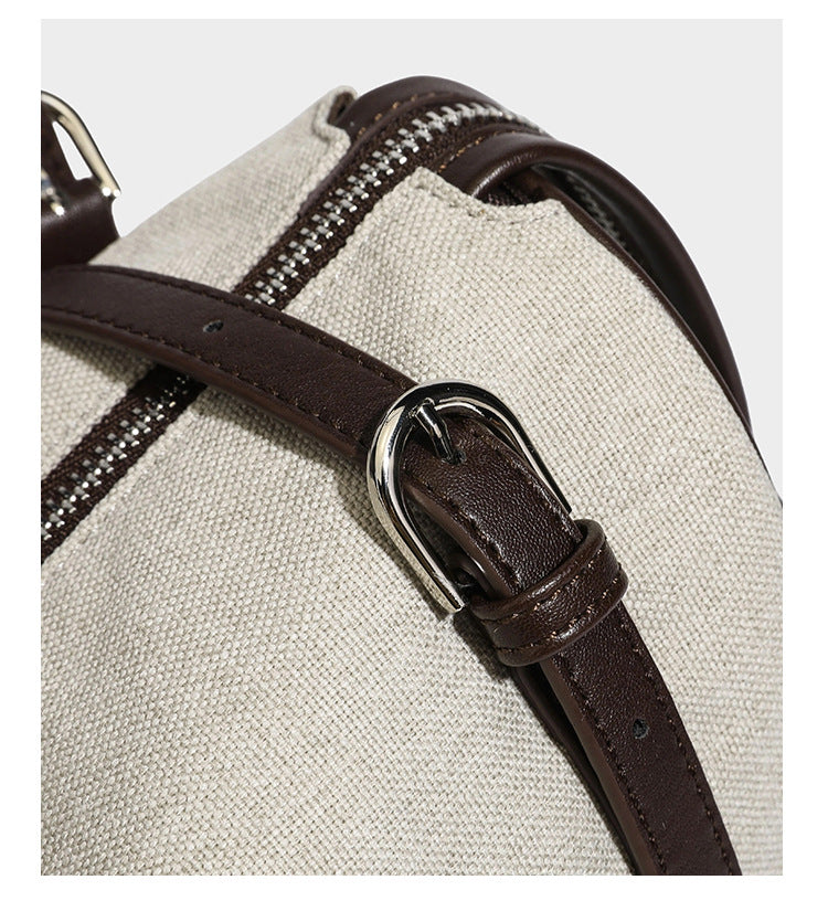 Beige canvas barrel bag with dark brown leather-look trim, silver-tone hardware, top zip closure, and adjustable shoulder