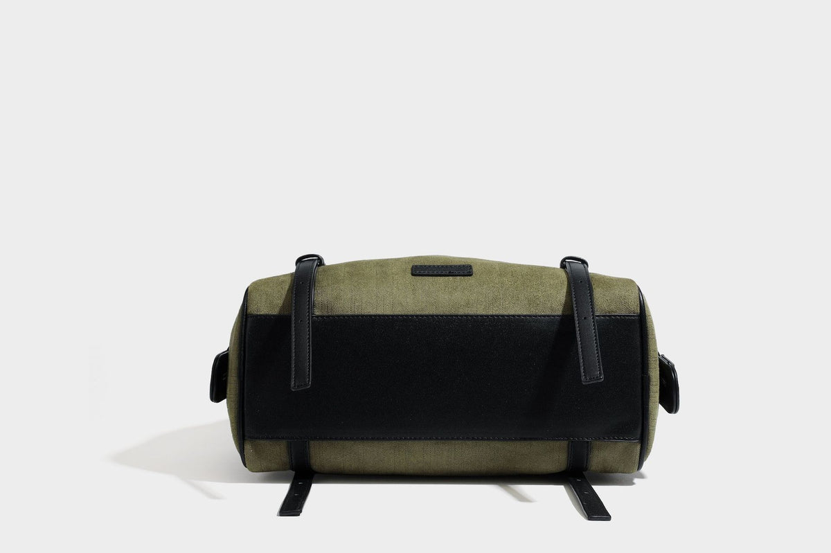Olivgrüne Canvas-Schultertasche in Zylinderform mit schwarzen Trägern in Lederoptik, Reißverschluss oben und silberfarbenen Metallbeschlägen, Detailansicht