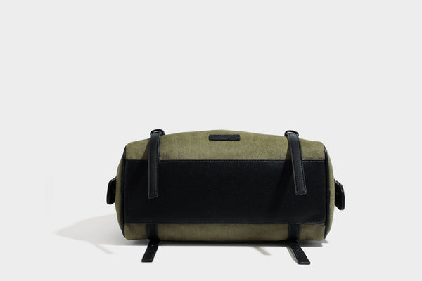 Olivgrüne Canvas-Schultertasche in Zylinderform mit schwarzen Trägern in Lederoptik, Reißverschluss oben und silberfarbenen Metallbeschlägen, Detailansicht