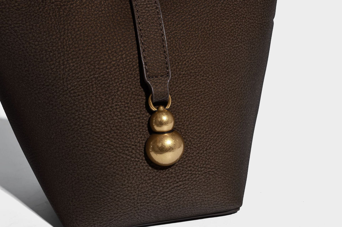 Kleine matte Beuteltasche mit genarbter Oberfläche, antikgoldfarbenen Ringbeschlägen, Perlen- und Quastenanhänger, kurzen Tragegriffen oben und