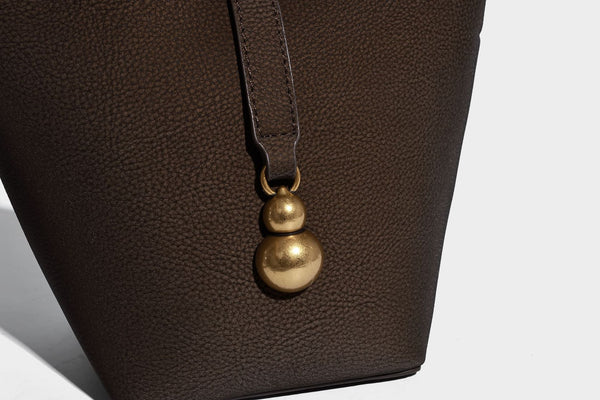 Kleine matte Beuteltasche mit genarbter Oberfläche, antikgoldfarbenen Ringbeschlägen, Perlen- und Quastenanhänger, kurzen Tragegriffen oben und