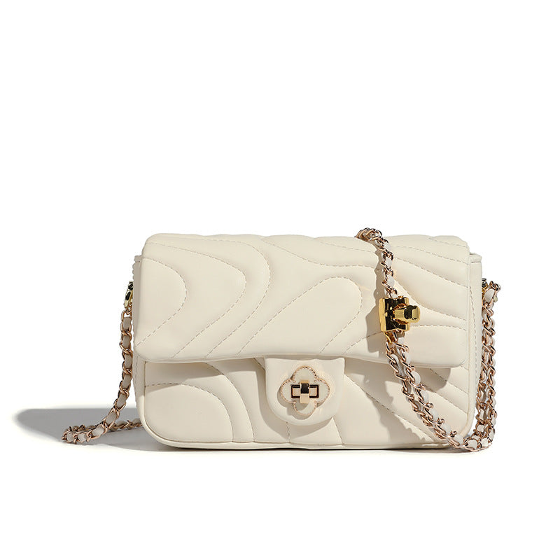 Compact cream quilted flap crossbody bag with wave stitching, gold-tone chain strap, and four-petal turn-lock clasp, detail