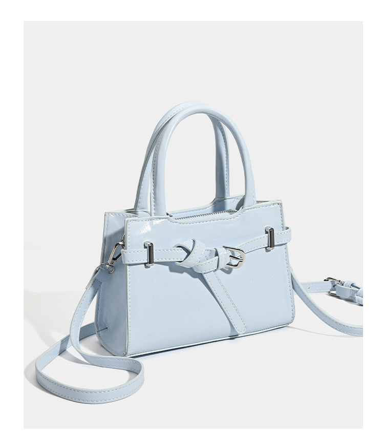 Small structured trapezoid mini top-handle bag with front belt-knot buckle detail and glossy leather-look finish, detail view