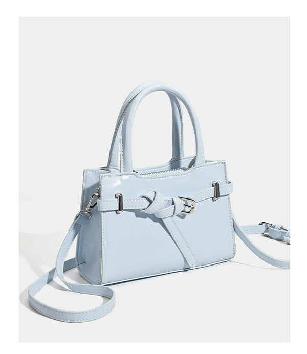Small structured trapezoid mini top-handle bag with front belt-knot buckle detail and glossy leather-look finish, detail view