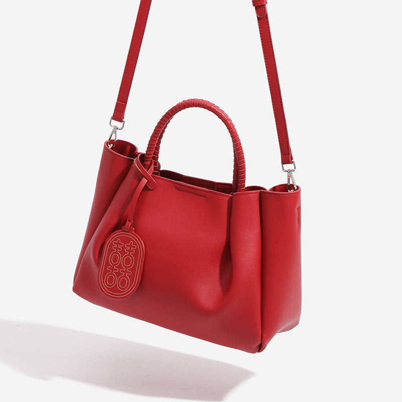 Structured matte red tote bag with coiled wrapped handles, double-happiness charm pendant, and removable grey zip inner