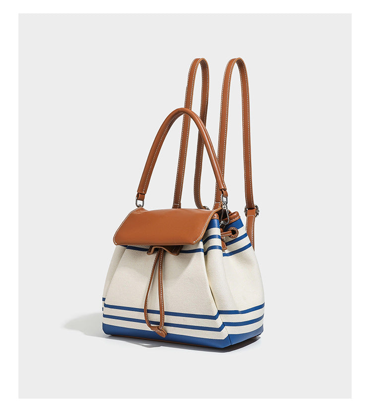 Cream canvas bucket bag with blue horizontal stripes, tan leather-look flap and trim, drawstring closure, silver-tone, detail