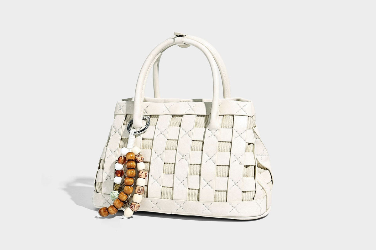 Small structured woven satchel tote with rounded top handles, silver-tone ring hardware, and bead tassel charm, detail view